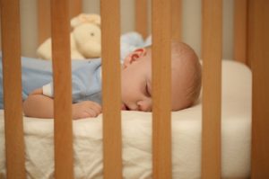 Young baby in a wooden crib. Unsafe, dangerous, and defective products. 