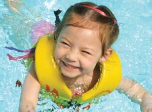 A young girl smiling while playing in a swimming pool while wearing a life preserver. Take precautions to prevent drownings, injuries and slip-and-fall accidents.