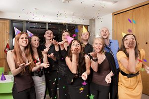 A happy group of people weating party hats while throwing confetti. Here are some safety tips for holiday shopping and company holiday office parties. 