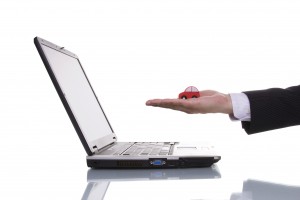 Man with hand extended holding small red car over a laptop