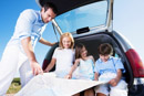 Family on vacation sitting in the back trunk area looking at a map. Here are a few tips to help make your family road trip a little safer and avoid auto accidents.