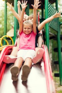 Happy kids slide on playground. Warm Weather Can Result In More Injuries On The Playground. 