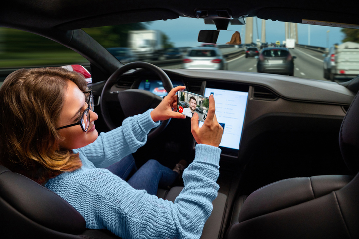Woman in an autonomous car texting on phone, hands off the wheel