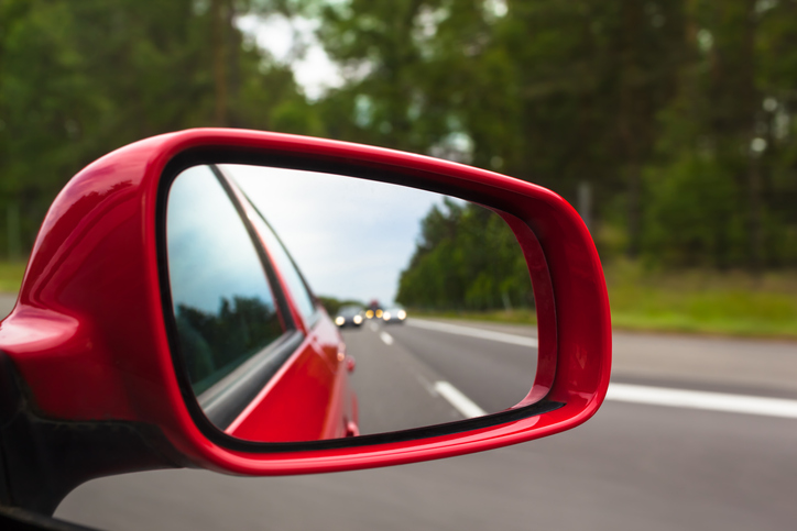 View back to road through red side mirror at car