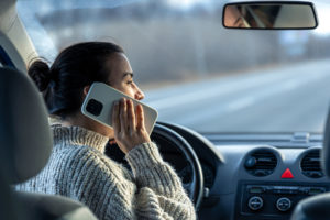 Young woman talking on the phone while driving a car, inside view.