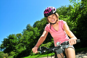 Young girl on bicycle wearing bike helmet.