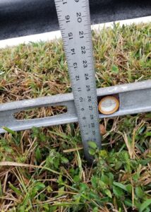 Trip and fall hazard, level and ruler showing depth and level of the hole covered by grass