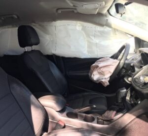 Inside view of the Ford Escape after collision. Extensive damage to drivers side windows, and front windshield and airbags deployed.