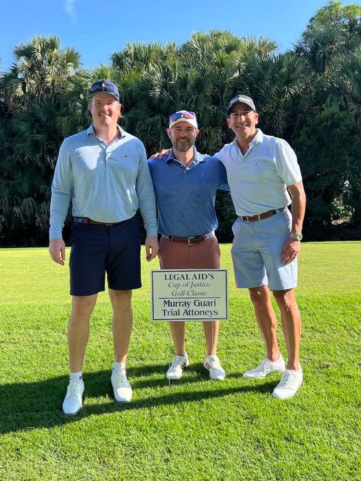 Attorneys Keith Hedrick, Scott Perry and Jason Guari near their sponsorship sign at the Legal Aid Society of Palm Beach County's Cup of Justice Golf Tournament