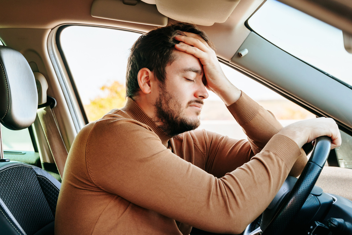 Side view young male driver closed his eyes and rests with his hand on the steering wheel and the other on his forehead. rest.