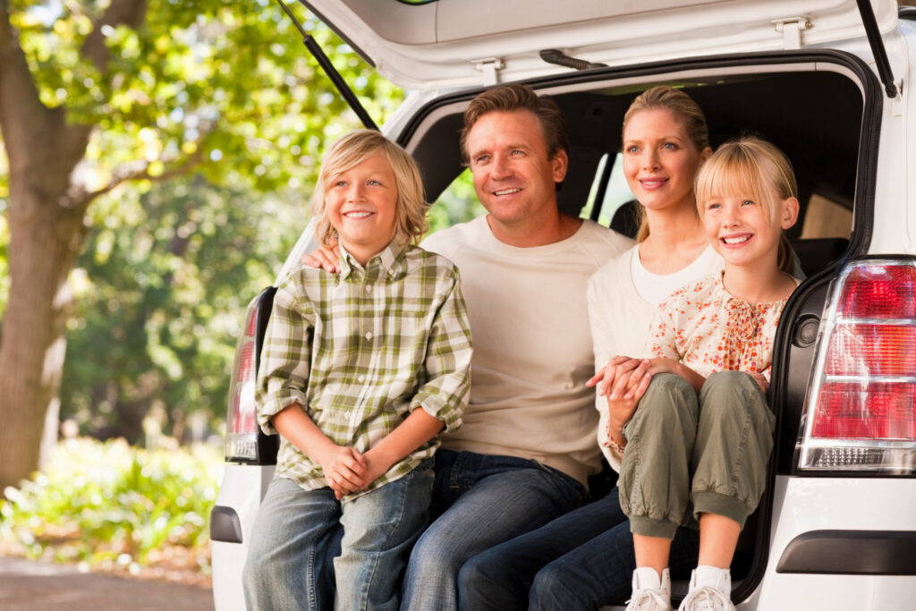 Happy family sitting together at the tailgate of a van while looking away